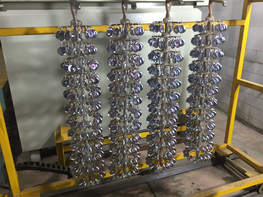 Every rack that leaves an electroplating bath carries a liquid film with it. Some solution sits on open surfaces. More remains around hooks, holes, seams, rack insulation, recesses, and horizontal ledges. If that liquid reaches the first rinse, the line loses metal salts and additives while the rinse system receives a higher contaminant load. An Air Knife can interrupt that loss at the tank boundary. Positioned over the correct bath or recovery area, it applies a controlled sheet of air as the work is withdrawn and drained. The liquid is pushed toward a known collection point and returned to the compatible process solution. The goal is recovery, not simply making the part look dry. Drag-Out Is Chemical Inventory Leaving the Bath  Electroplating drag-out is not just water on a part. It may contain nickel, copper, zinc, chromium compounds, acids, alkalis, complexing agents, brighteners, wetting agents, or other bath constituents. The cost appears in several places: fresh chemical makeup, rinse-water demand, wastewater treatment, sludge, bath imbalance, and contamination of later stages. The loss rate changes with bath viscosity, surface tension, temperature, withdrawal speed, drainage time, rack orientation, part geometry, and barrel condition. A flat coupon drains differently from a threaded casting. A rack with damaged insulation can hold solution in cracks even when the parts themselves drain well. For this reason, air knife performance should be measured by recovered liquid and reduced rinse loading, not by outlet velocity alone. Put the Air Knife Inside the Recovery Boundary For direct recovery, install the air knife over the plating tank or over a drainboard that slopes back to that same tank. The work should not cross above an unrelated bath while concentrated solution is being removed. Splash guards, drip trays, and exhaust capture must keep the displaced liquid and mist inside the intended boundary. The first rinse is a different location with a different objective. Blow-off there may reduce carryover into the next rinse, but that liquid is already diluted and may not be suitable for direct return to the plating bath. Mark each knife in the line by source chemistry, approved destination, and operating recipe. This prevents a useful recovery device from becoming a cross-contamination path. The Four-Part Air Knife Removal Sequence 1. Controlled Withdrawal Lift the work smoothly. Fast withdrawal leaves a thicker liquid film, while abrupt acceleration shakes droplets outside the tank. On automated hoists, tune the lift profile for the highest-drag-out product family rather than using one aggressive motion for every rack. 2. Gravity Drainage Pause over the bath long enough for major streams to stop. EPA guidance has documented large drag-out reductions from longer drainage and slower withdrawal, but excessive dwell can create dry-on marks or process delays. The correct time comes from a line trial, not a universal timer value. 3. Directed Airflow Start the air knife after the heavy runoff has fallen. Aim the air curtain toward the return zone and sweep from the upper liquid edge toward the lowest drain point. Too much force atomizes solution, loads the exhaust system, and can blow chemistry onto bus bars or adjacent tanks. 4. Captured Return Keep the part above the source tank or sloped drainboard until displaced liquid has cleared. The return path must be clean, chemically compatible, and free of debris. A knife that moves liquid off the work but sends it to the floor or first rinse has not reduced the chemical loss. Air Knife Setups for Rack Plating, Barrel Plating, and Flat Work  Rack-plated parts usually need coverage from more than one direction. Hooks, shielded rear faces, nested components, and pockets can sit outside a single air curtain. Two opposed knives or a staged top-to-bottom sweep may be needed, but the jets should not collide and create uncontrolled mist. Racks also need regular inspection for cracked insulation and metal buildup that forms liquid pockets. Barrels retain solution in perforations, end plates, internal parts, and plugged holes. Rotation in the upright drain position often matters more than a stationary external jet. Use the air knife as part of the withdrawal-and-rotation sequence, and verify that air reaches the drainage path without driving aerosol through the enclosure. Panels, strip, wire, and other continuous products give a more repeatable target. A narrow, angled air curtain can push the liquid line back toward the tank. Two-sided products may need upper and lower knives, balanced so the lower jet does not lift the strip, disturb electrical contact, or throw liquid beyond the capture zone. Recovery Must Protect the Plating Chemistry Returning solution is valuable only when the return is chemically acceptable. Confirm that the recovered liquid comes from the same bath and has not collected rinse water, cleaner, etchant, oil, particles, or corrosion debris. Some baths tolerate direct return; others require filtration, concentration control, or a separate recovery rinse. Electroless and tightly controlled baths can be especially sensitive to unwanted contaminants. Also review the bath volume balance. A hot bath with normal evaporation may accept recovered solution more easily than a low-evaporation bath already near its operating level. Coordinate air knife recovery with makeup water, level control, filtration, and analytical additions. Recovery should stabilize the process, not gradually overfill or dilute it. Air Knife Control of Mist, Air Quality, and Surface Risk Plating solution can be hazardous and corrosive. The exhaust hood must capture the mist created during blow-off without pulling the air curtain away from the work. Test with the enclosure operating at its normal extraction rate. Add shields where the stream can strike edges, holes, or fixtures and break into droplets. The supplied air must not add oil, condensate, rust, or particles to a freshly plated surface. Use suitable filtration and drain the air system. Blower-driven air is often preferred for continuous coverage and energy control, while compressed air may fit short, intermittent, or highly localized tasks. In either case, confirm the cleanliness required by the plating finish and the next process step. Do not chase a completely dry surface if the process cannot tolerate it. Rapid drying can leave salts, stains, or dry-on patterns, and some downstream coatings require a clean, active surface. Define the acceptable endpoint as reduced transferable solution with no finish damage, not “maximum air.” QXY Air Knife Starting Specifications for Electroplating Lines These values are engineering starting points for blower-driven systems, not final settings. QXY Machinery should review the actual chemistry, rack envelope, wet width, exhaust arrangement, and return geometry before selection. Design item	QXY starting point	Why it matters on a plating line Body material	PVC for many low-temperature acidic or alkaline wet zones; verify exact chemistry	Reduces corrosion risk near plating and rinse tanks without paying for a premium alloy where it is not needed Blower pressure	2–6 psi (0.14–0.42 bar) at the knife inlet	Supports a continuous air curtain; final pressure must be set by runoff and mist tests Working distance	20–50 mm from the target surface	Keeps useful impact while leaving clearance for racks, hooks, and part variation Impingement angle	15°–45° from the surface, aimed toward the approved return zone	Moves liquid in a controlled direction instead of atomizing it across the line Slot and width	0.5–2 mm standard slot; standard lengths 150–1,000 mm; custom lengths available	Matches the wet width and liquid load; wider openings require enough blower flow Inlet arrangement	Dual inlets normally used above 600 mm	Helps maintain coverage across wide panels, long racks, or strip lines  PVC is often a practical body material near low-temperature acid, alkaline, plating, and rinse environments. It is light and economical, but its suitability depends on chemical type, concentration, temperature, exposure time, pressure, impact, and mounting span. Stainless steel or titanium may be better where temperature, load, or documented corrosion conditions exceed the PVC operating window. Commission the Air Knife with a Mass-Balance Test Begin with the existing line. For a representative rack or barrel load, measure drip time, first-rinse conductivity or chemistry, bath makeup, and visible runoff pattern. Then run the same product with the air knife operating. Keep production rate, withdrawal profile, bath condition, and rinse flow as constant as possible. Collect returned liquid where practical, or use bath-level and concentration records over enough cycles to smooth out normal variation. Check the first rinse for reduced contaminant loading. Inspect the plated surface under the normal quality standard for stains, residue, roughness, adhesion problems, or marks caused by rapid drying. •Confirm that all displaced liquid reaches the approved tank or recovery vessel. •Record pressure, slot setting, distance, angle, hoist speed, drain time, and exhaust state. •Test the worst-draining rack and the most sensitive finish, not only a flat sample. •Look for mist on tank rims, bus bars, sensors, floors, and neighboring stages. •Recheck rinse loading and chemical makeup after a stable production period. Maintenance Determines Whether Savings Continue Inspect the slot for salt buildup and verify that airflow remains even across the wet width. Check brackets, shields, hoses, blower filters, drains, and the sloped return surface. A shifted angle or blocked drain can quietly redirect recovered chemistry away from the process tank. Include the system in plating-line change control. A new part family, rack design, bath chemistry, concentration, temperature, hoist program, or exhaust setting can change the liquid path. Repeat the runoff and rinse-loading checks after any change that affects drainage or airflow. About QXY Machinery QXY Machinery (Shenzhen Qixingyuan Machinery Equipment Co., Ltd.) is a high-tech enterprise integrating R&D, design, production, and sales. Based in Shenzhen, China, the company has more than 10 years of focused air knife experience for industrial drying, liquid removal, dust control, and wet-process equipment. For electroplating and surface-treatment lines, QXY Machinery supplies PVC, 304 and 316 stainless steel, titanium alloy, aluminum alloy, slot, small-hole, and dual-sided air knife configurations. Length, slot width, inlet direction, mounting, material, and air source can be matched to the tank layout and work envelope. A useful application request includes the plating chemistry, concentration, temperature, rack or barrel drawing, wet width, withdrawal motion, drain time, exhaust arrangement, available air source, return destination, and surface-quality limit. → Contact QXY Machinery to review an air knife system for electroplating drag-out recovery. FAQ Q: Where should an air knife be installed to reduce electroplating drag-out? A: For direct recovery, place it over the source plating bath or a drainboard that returns to that bath, before the work enters the first rinse. Q: Can an air knife replace drainage time over the plating tank? A: No. Slow withdrawal and gravity drainage remove the heavy liquid first. Airflow should handle the remaining film and droplets inside the recovery zone. Q: How much can air knives reduce chemical drag-out? A: Results depend on geometry, bath properties, withdrawal, drainage, airflow, and capture. EPA material reports a 75% reduction at one facility, but each line needs its own baseline and mass-balance test. Q: Is PVC suitable for an electroplating air knife? A: PVC can suit many low-temperature acidic, alkaline, plating, and rinse environments. Confirm the exact chemical, concentration, temperature, exposure time, pressure, and structural load. Q: Will higher air pressure always recover more plating solution? A: No. Excess force can create mist, scatter chemistry, and damage surface quality. Use the lowest setting that moves liquid consistently into the approved return path. Q: Can recovered solution always be returned to the plating bath? A: Only when the chemistry owner approves the source, cleanliness, concentration, and volume balance. Some solutions require filtration, analysis, or a separate recovery step. Q: How is drag-out reduction verified after installation? A: Compare representative production before and after installation using rinse loading, returned-liquid measurements, bath makeup, chemical balance, mist inspection, and plated-surface quality.